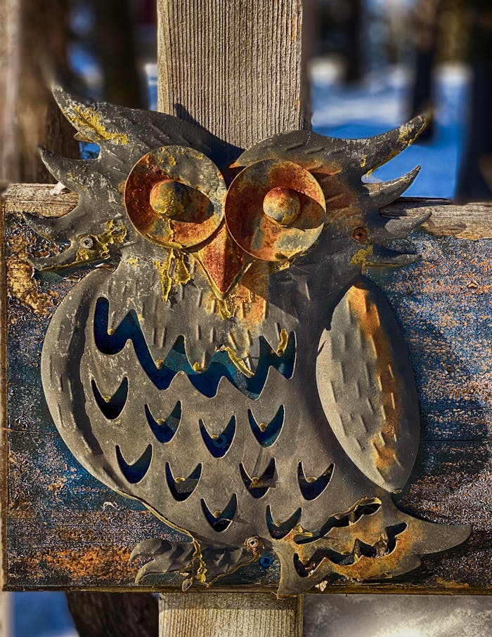 A rustic metal owl decoration on a wooden post captures the afternoon sun outdoors.